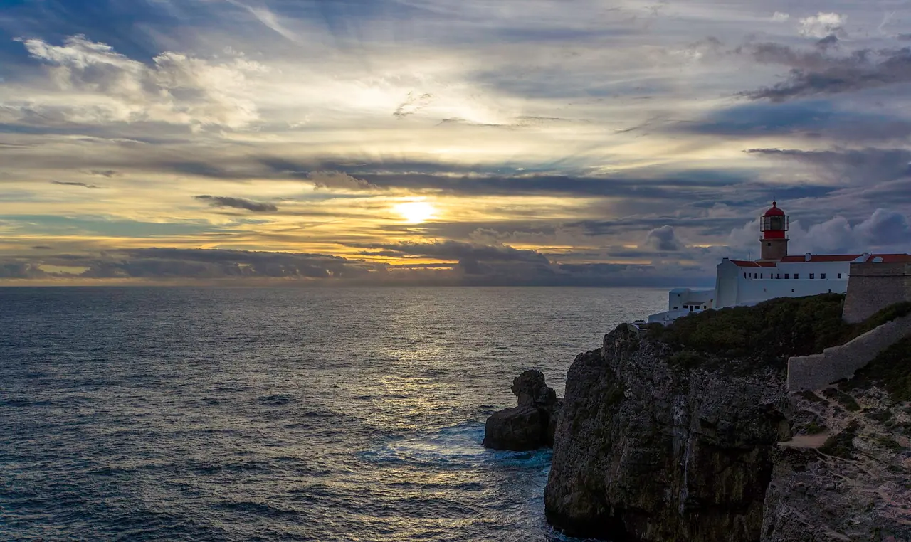 Der rot-weiße Leuchtturm am Cabo de São Vicente auf der Klippe, davor das Meer im Licht des Sonnenuntergangs