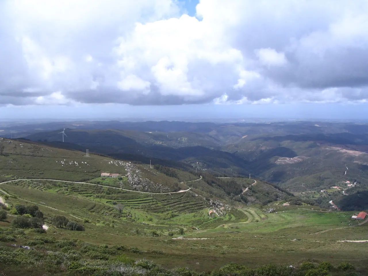 Weiter Blick in die Serra de Monchique mit terrassierten grünen Hängen unter einem Himmel mit großen Wolken