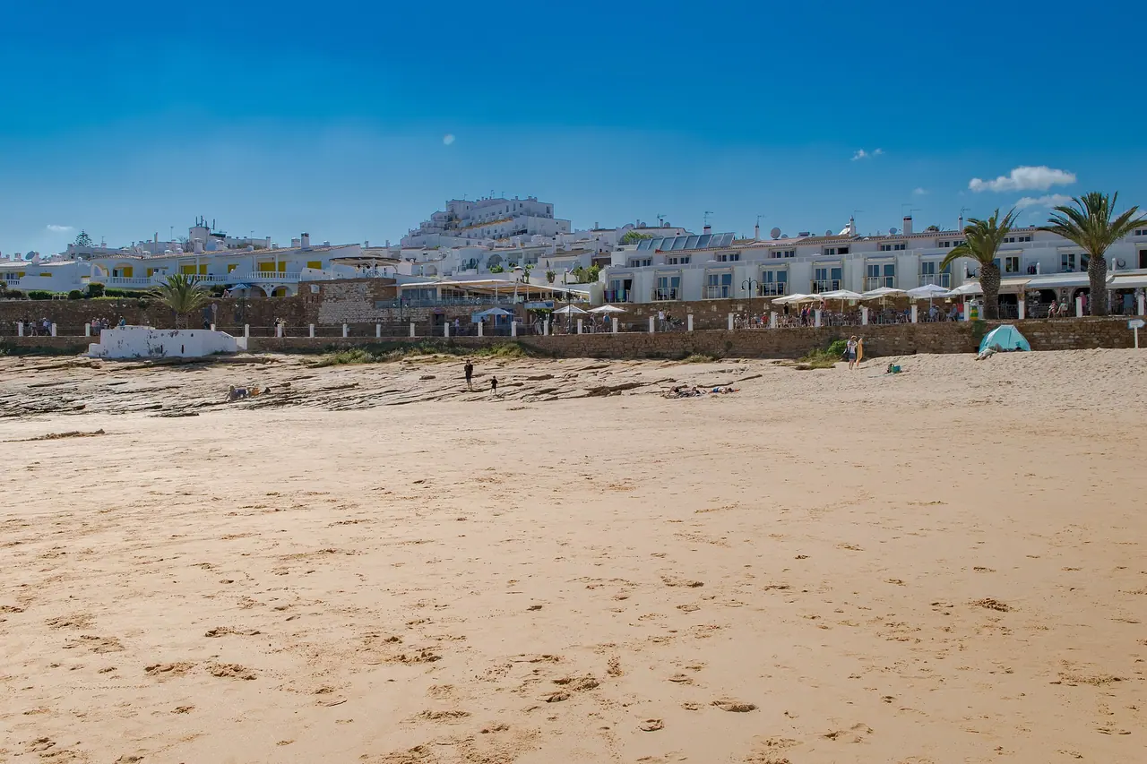 Breiter Sandstrand von Praia da Luz mit Palmen und weißen Häusern der Strandpromenade unter blauem Himmel
