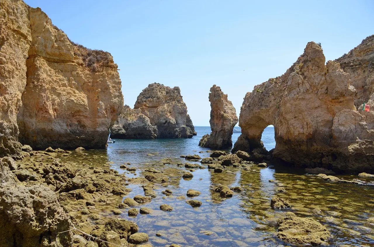 Felsentor und Felsnadeln aus goldgelbem Sandstein an der Ponta da Piedade, dazwischen ruhiges Wasser im Flachen