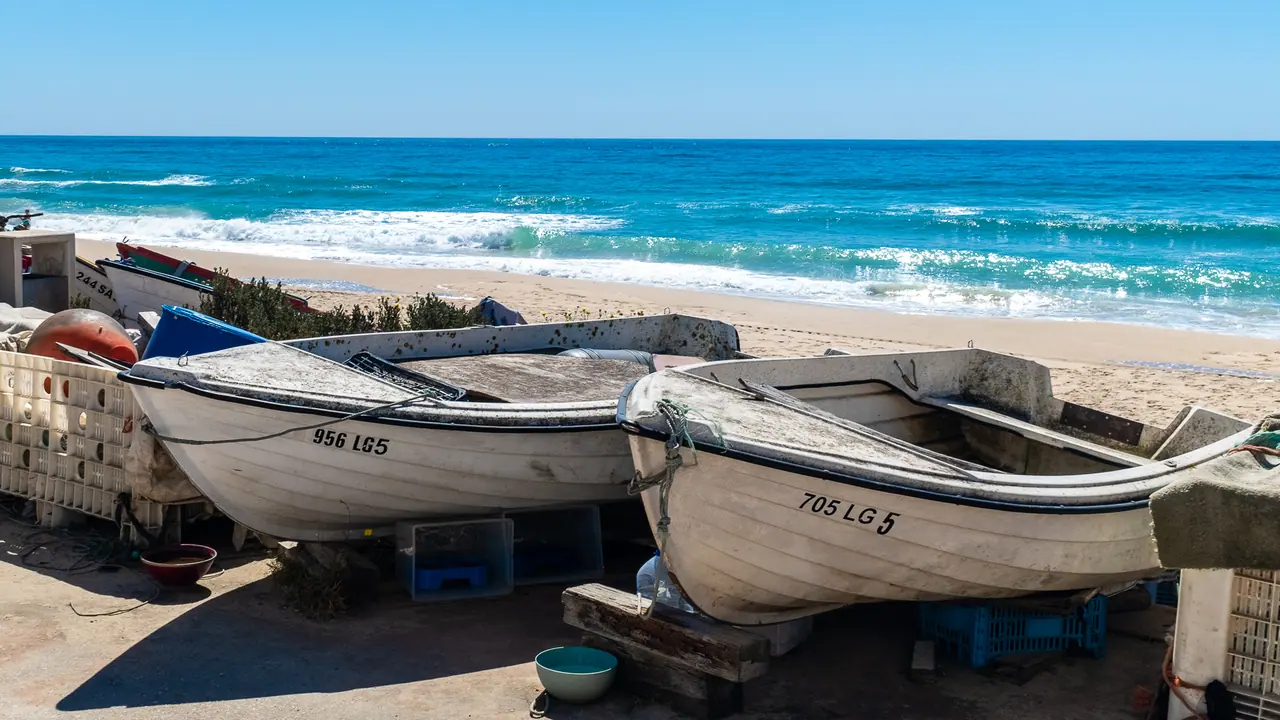 Zwei weiße Fischerboote auf dem Strand von Salema, dahinter Brandung und das türkisfarbene Meer